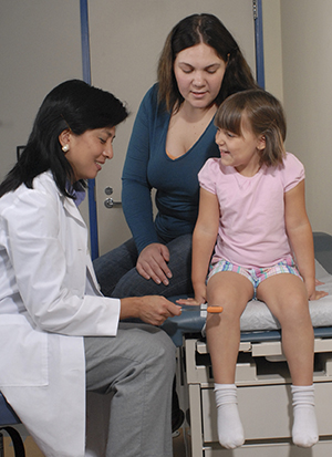 Healthcare provider testing girl's knee reflex in exam room. Woman sitting behind girl.