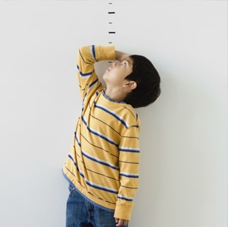 Toddler measuring themself with a drawn ruler on a wall.